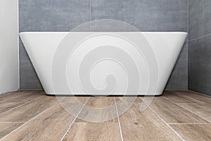A modern, free-standing wall-mounted bathtub, without a tap, standing in a bathroom lined with ceramic tiles.