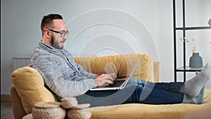 Modern freelancer bearded guy working remotely use laptop pc on yellow couch. 4k Dragon RED camera