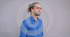 Modern freelancer with ponytail watches thoughtfully sidewards turns to camera on gray wall background.