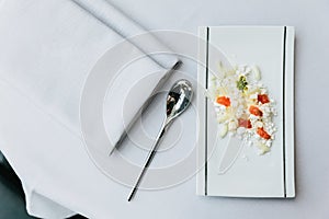 Modern French appetizer: crush and cut cheese with diced tomato served on white rectangle plate with silver spoon and napkin