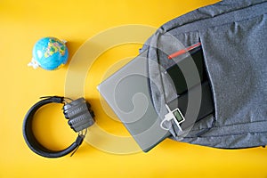 Modern gadgets: laptop, smartphone and external battery in a textile backpack next to a small globe and headphones. Yellow