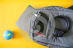 Modern gadgets smartphone, external battery and laptop lie in fashionable textile backpack next to  small globe. Yellow background