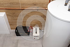 Modern gas boiler room lined with ceramic tiles imitating wood, visible emergency power supply with a 12 volt battery.