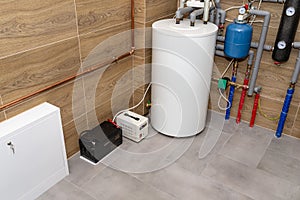 Modern gas boiler room lined with ceramic tiles imitating wood, visible emergency power supply with a 12 volt battery.