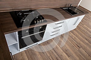 A modern gas cooker with ceramic hob, electric oven and a dark brown wooden kitchen with wash-basin ready for cooking a meal