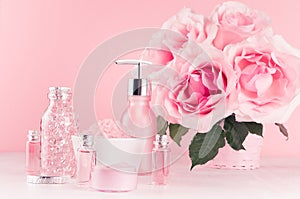 Modern gentle girlish bathroom decor - cosmetics for bath, spa, bouquet of roses, bath accessories on soft white wooden table.