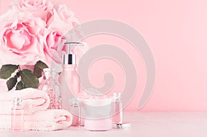 Modern gentle girlish bathroom decor - cosmetics for bath and spa, bouquet of roses, bath accessories on soft white wooden table.