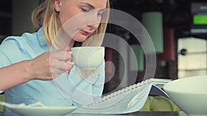 Modern girl in a cafe drinking tea, uses the tablet and writes in notebook. Beautiful girl in the coffee shop working or