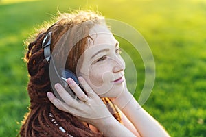 Modern girl with dreadlocks listening to music with her headphones in autumn Sunny Park. Melomania and good mood