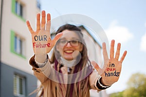 Modern girl with long dreadlocks and eyeglasses in nude color trench is showing hands with written slogan `Our future in