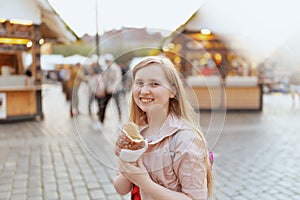 modern girl in pink jacket at fair in city eating trdelnik
