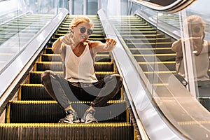 Modern girl sitting on an escalator with her arms raised jokingly