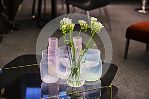 Modern glass vases in different shades, pink, white, blue, with flowers standing in the interior