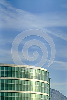 Modern glass wall round building exterior against mountain and cloudy blue sky