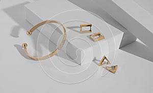 Modern gold bracelet and geometric earrings on white podium with copy space