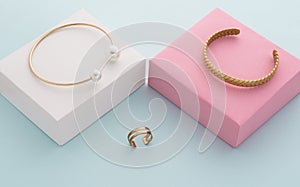 Modern golden bracelets on pink and white boxes and double shape ring on blue background