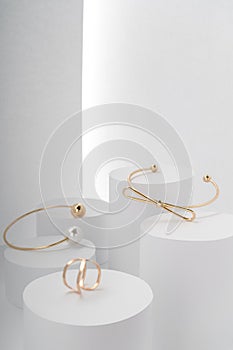 Modern golden bracelets and golden ring on white round platforms