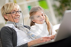 Modern grandmother teaching grandchild how to use laptop