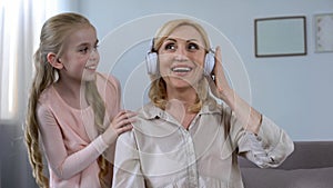 Modern granny in headphones listening to favourite song of her granddaughter