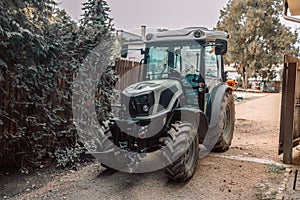 Modern green good-looking tractor stands in outside garage near agricultural fixtures and transport on farm or ranch on