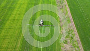 Modern green tractor spraying wheat field with chemicals fertilizers in cloudy spring day