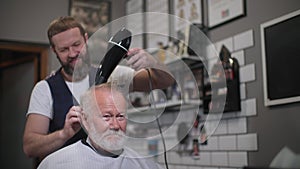 modern hair stylist gives a haircut to stylish elderly male client and blow-dry his hair while styling with hairdresser