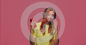 Modern happy young girl in wireless headphones dancing, enjoy listening to disco music in mobile phone application