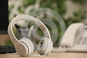 Modern headphones, desktop telephone and computer on table indoors