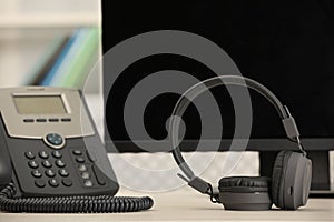 Modern headphones, desktop telephone and computer on table indoors