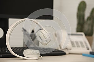 Modern headphones, desktop telephone and computer on table indoors, space for text