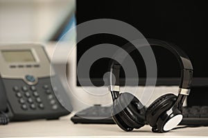 Modern headphones, desktop telephone and computer on table indoors, space for text