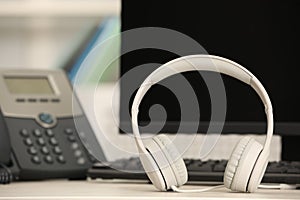 Modern headphones, desktop telephone and computer on table indoors, space for text