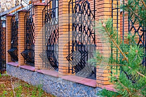 Modern, high, beautiful Fence with steel rods and pillars of brick.