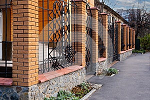 Modern, high, beautiful Fence with steel rods and pillars of brick.