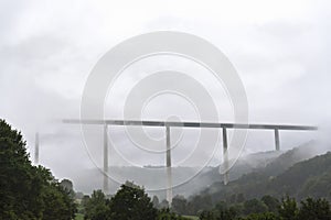 Modern high bridge over wooded hills and fog