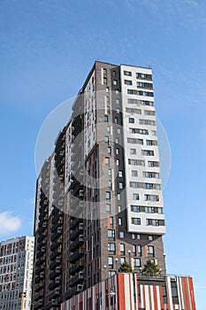 A modern high-rise building against a blue sky. New modern construction. Green trees on the roof