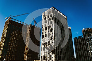 Modern high-rise buildings under construction and cranes against a blue sky. Urban background. Urban sprawl concept