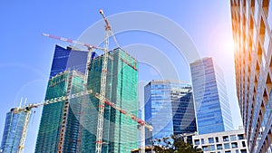 Modern high-rise buildings under construction next to glass skyscrapers in background.