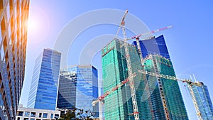 Modern high-rise buildings under construction next to glass skyscrapers in background.