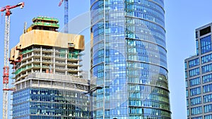 Modern high-rise buildings under construction next to glass skyscrapers in background.