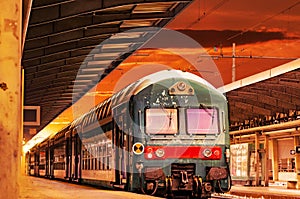 Modern high speed commuter train at the railway station at colorful sunset with vintage toning