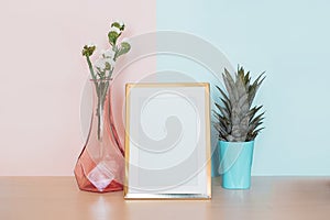 Modern home decor mock up with gold blank photo frame, vase and tropical plant on pink blue background