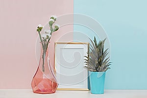 Modern home decor mock up with gold blank photo frame, vase and tropical plant on pink blue background