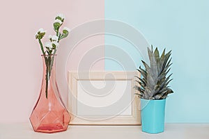 Modern home decor mock up with wooden blank photo frame, vase and tropical plant on pink blue background
