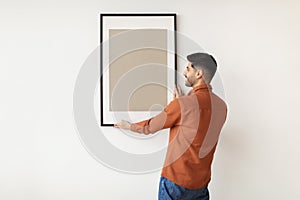 Young man hanging picture frame on the wall