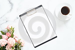 Modern home office desk workspace with blank paper clipboard mockup, pink roses flower bouquet, coffee cup on white marble stone