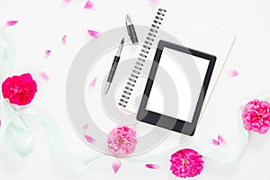 Modern home office desk workspace with blank screen tablet e-book, feminine accessories, blue mint ribbon, pink rose flower buds