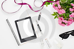 Modern home office desk workspace with blank screen tablet e-book, feminine accessories, glasses, paper notebook, bouquet of pink
