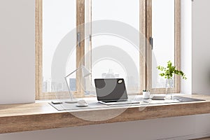 Modern home office with wooden tabletop, modern laptop, city view from the window, white coffee mug and lamp and glass vase