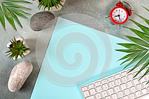 Modern home office workplace with empty blue paper. A fragment of keyboard, home flowers, stones and clock watch on a table.